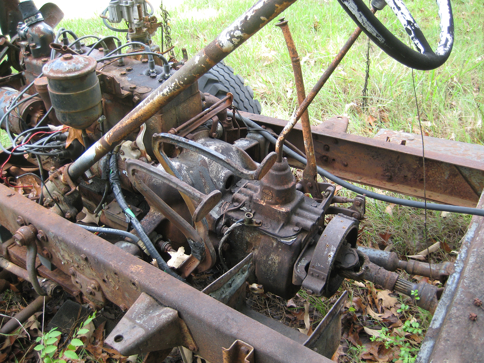 Rusted steering wheel and pedals with engine block and chassis of a 1941 Army Command Car.