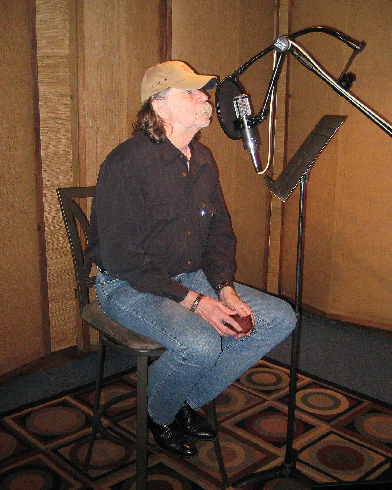 Colonel sitting on a stool, talking into a recording mic in a studio.