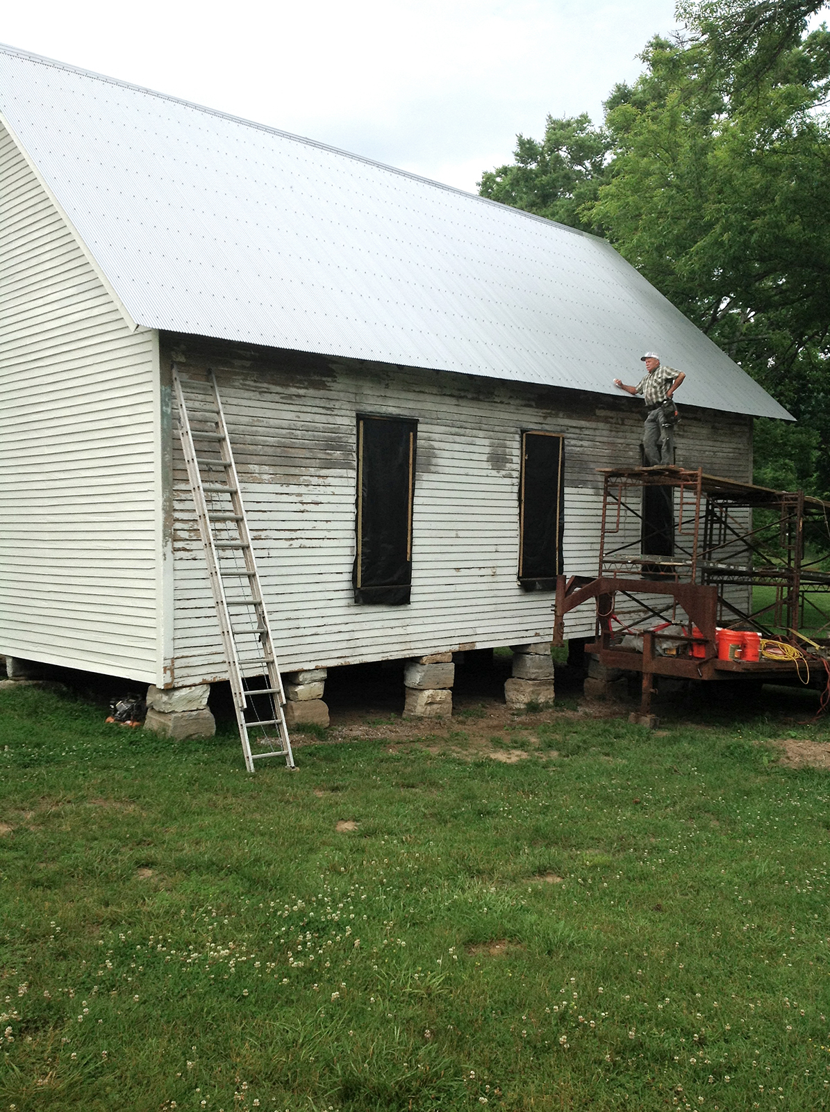 Payton Hewitt on scaffolding leaning against completed roof of one-room schoolhouse on Foxfire Farm in Lynnville, TN
