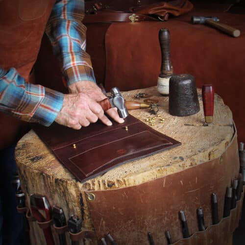 Man working with hand leather tools on an antique wood stump work station