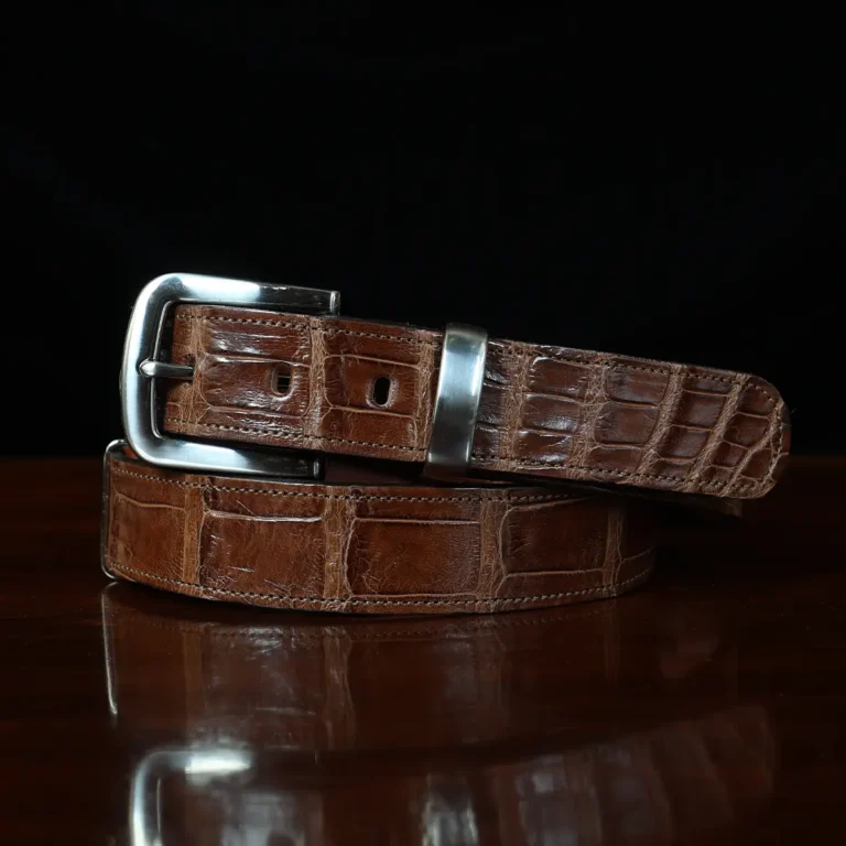 An American Alligator Belt with Nickel hardware showing the front view on a wooden table with black background