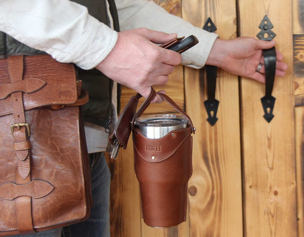 Leather tumbler sleeve for 30 ounce Yeti Rambler cup one finger carrying sleeve by handle heading out the door.